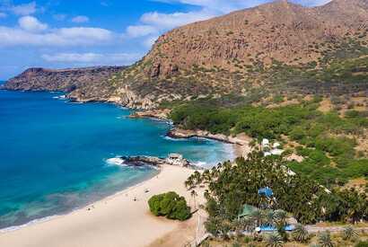 Feinsandiger Strand mit Palmen und türkisblauem Wasser in Tarrafal auf Santiago, Kapverden, eingerahmt von Bergen.