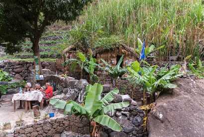 Touristen genießen eine Mahlzeit im Grünen vor einer traditionellen Hütte auf Santo Antão, Kapverden – ein Beispiel für nachhaltigen und respektvollen Tourismus.