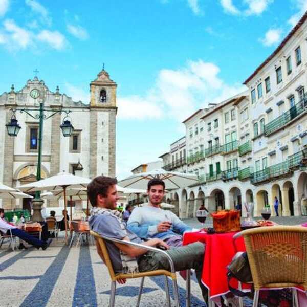 Besucher genießen ein Café auf dem Praça do Giraldo vor der historischen Kulisse der Altstadt von Évora im Alentejo.