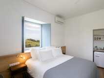 Solar Branco Eco Estate auf Sao Miguel, helles und modernes Zimmer mit gemütlichem Bett und Blick auf die grüne Natur – nachhaltiger Komfort im Einklang mit der Umgebung.