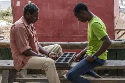 Zwei Männer auf den Kapverden spielen das traditionelle Brettspiel „Oware“ an einem Holztisch.