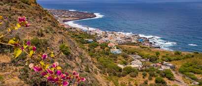 Blick von einem Hügel auf die Stadt São Filipe und die Küste von Fogo mit blühender Bougainvillea im Vordergrund