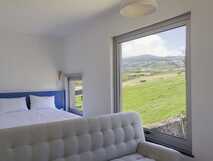 Loft Azul Pastel Hotel auf Faial, modernes Zimmer mit gemütlichem Bett und großem Fenster mit weiten Ausblicken auf grüne Landschaft.