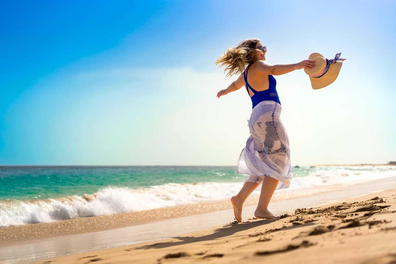 Urlauberin tanzt barfuß an einem sonnigen Sandstrand auf den Kapverden.