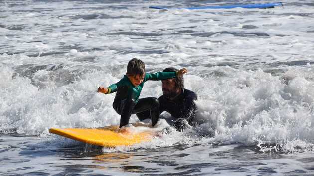 Kleiner Junge auf dem Surfbrett - erste Stehversuche. Ein Mann hält das Board.