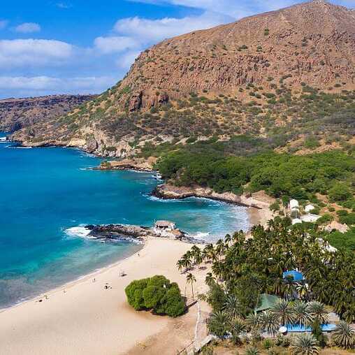 Feinsandiger Strand mit Palmen und türkisblauem Wasser in Tarrafal auf Santiago, Kapverden, eingerahmt von Bergen.