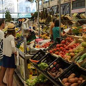 Touristen beim Einkauf von frischem Obst und Gemüse auf einem Markt in Portugal.