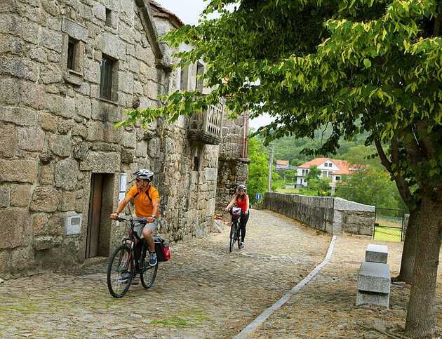 Zwei Radfahrer radeln durch einen Ort mit dicker Mauer und genießen das Flair des geschichtsträchtigen Gemäuers: Typisch Portugal