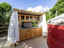 Azul Singular auf der Insel Faial, Außenküche mit Holzfronten neben einem roten Rundzelt, umgeben von grüner Vegetation.
