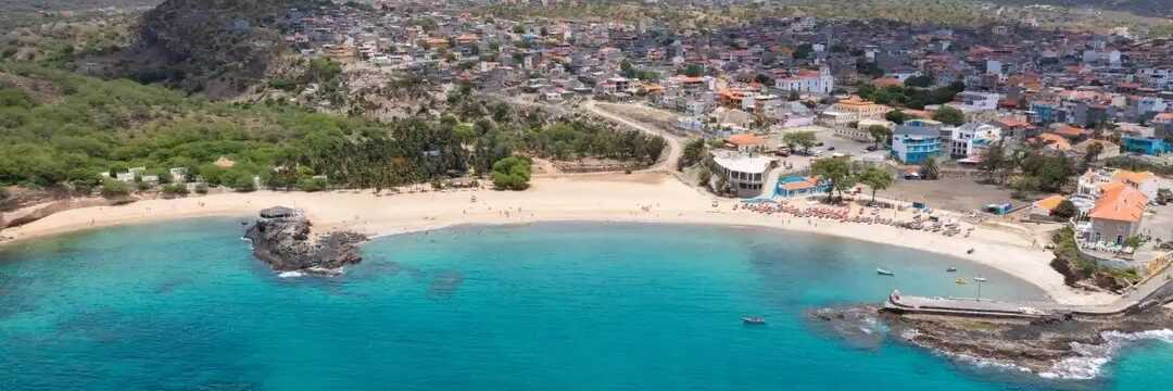 Luftaufnahme der Bucht von Tarrafal mit weißem Sandstrand, türkisfarbenem Wasser und Palmenkulisse auf Santiago, Kapverden.
