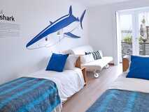 Casa da Baia auf Faial – helles, freundliches Zimmer mit zwei Einzelbetten, blauen Akzenten und einer Wandillustration eines blauen Hais.