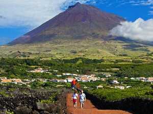 Wanderer auf einem roten Pfad inmitten grüner Landschaft mit dem majestätischen Pico-Vulkan im Hintergrund auf der Azoreninsel Pico