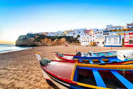 Ein Strand mit bunten Fischerbooten und ein Fischerdörfchen im Hintergrund, an der Küste von Portugal im Süden, an der Algarve.