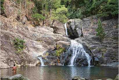 Kleiner Wasserfall mit Naturbecken inmitten grüner Wälder in Nordportugal, ein Wanderer steht im Wasser.