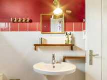 Estrela do Atlantico auf Faial, Badezimmer mit weißem Waschbecken, roten und weißen Fliesen, Spiegel und hölzernen Ablagen.