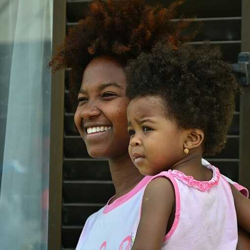 Kapverdische Mutter mit ihrem Kind im Arm, beide lächeln in die Kamera.