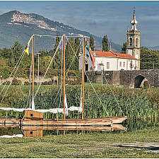 Nachgestellte Szene mit römischer Statue, Flussboot und Kirche in Ponte de Lima vor Bergkulisse.