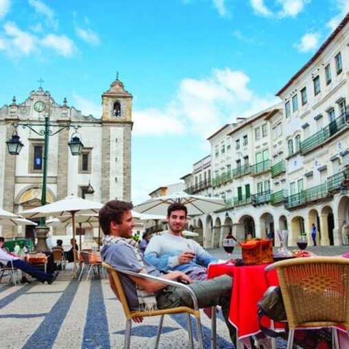 Besucher genießen ein Café auf dem Praça do Giraldo vor der historischen Kulisse der Altstadt von Évora im Alentejo.