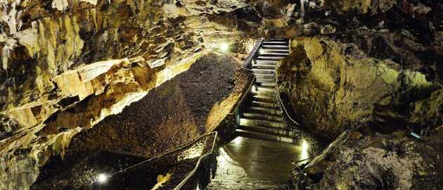 Begehbarer Innenraum des Algar do Carvão auf Terceira (Azoren): Treppen und Stege führen durch den vulkanischen Förderschlot und machen die Schichtung des basaltischen Gesteins sichtbar.