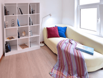 Casa da Baia auf Faial, gemütlicher Lese- und Entspannungsbereich mit einem hellen Sofa, bunten Kissen, einem bunten Plaid und einem Bücherregal in einem modernen, lichtdurchfluteten Raum.