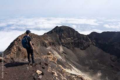 Wanderer steht am Rand des Kraters des Pico do Fogo auf den Kapverden und blickt auf die felsige Vulkanlandschaft.