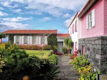 Innenhof der Quinta da Meia Eira mit rosa Hausfassade, weißen Fensterläden und üppigem Garten vor blauem Himmel