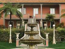 Außensicht der Villa Camelia mit prächtiger Fassade, Palmen und einem mehrstufigen Brunnen im Garten