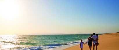 Familie spaziert am goldenen Sandstrand des Alentejo bei Sonnenuntergang – entspannter Familienurlaub am Meer in Portugal.