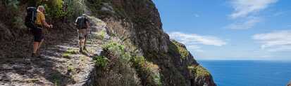 Zwei Wanderer auf einem schmalen Küstenpfad an der Levada do Norte mit Blick auf den Ozean