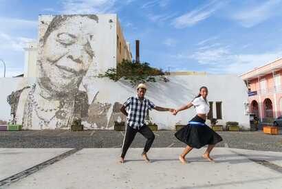 Tanzendes Paar auf einem Platz in Mindelo vor einem Wandbild mit lachendem Gesicht auf São Vicente, Kapverden.