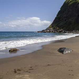 Strand mit schwarzem Sand und Felsen am Meer vor grünem Küstenhügel – idyllisches Naturparadies entdecken mit picotours.