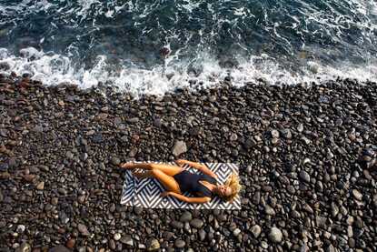 Vogelperspektive auf eine Frau, die entspannt auf dem Rücken an einem Steinstrand auf Madeira liegt