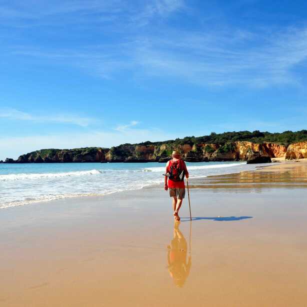 Mann wandert mit Wanderstab am Strand entlang