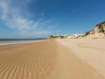 Weitläufiger Sandstrand unter blauem Himmel mit malerischer Küstenlandschaft – Ihr perfektes Urlaubsziel mit picotours.