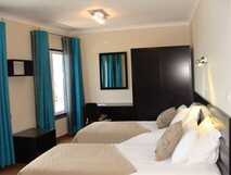 Apartaments Kosmos auf der Insel Faial, modern eingerichtetes Doppelzimmer mit zwei Einzelbetten, blauen Vorhängen und schlichter Dekoration.