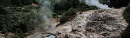 Dampf steigt aus einer heißen Schwefelquelle im Kurort Furnas auf São Miguel empor, umgeben von grünen Hügeln.