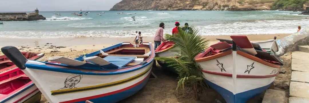Bunte Fischerboote am Strand von Tarrafal auf Santiago, Kapverden – mit Blick auf die malerische Bucht und Berge im Hintergrund.