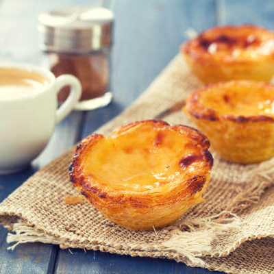 Drei Pastéis de Nata auf Leinentuch mit einer Tasse Espresso – portugiesisches Dessert.