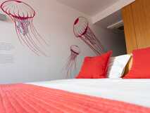 Casa da Baia auf Faial, gemütliches Hotelzimmer mit weißer Bettwäsche, roten Kissen und Wanddekoration mit roten Quallen.