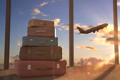 Ein Stapel Koffer am Flughafen mit startendem Flugzeug im Hintergrund