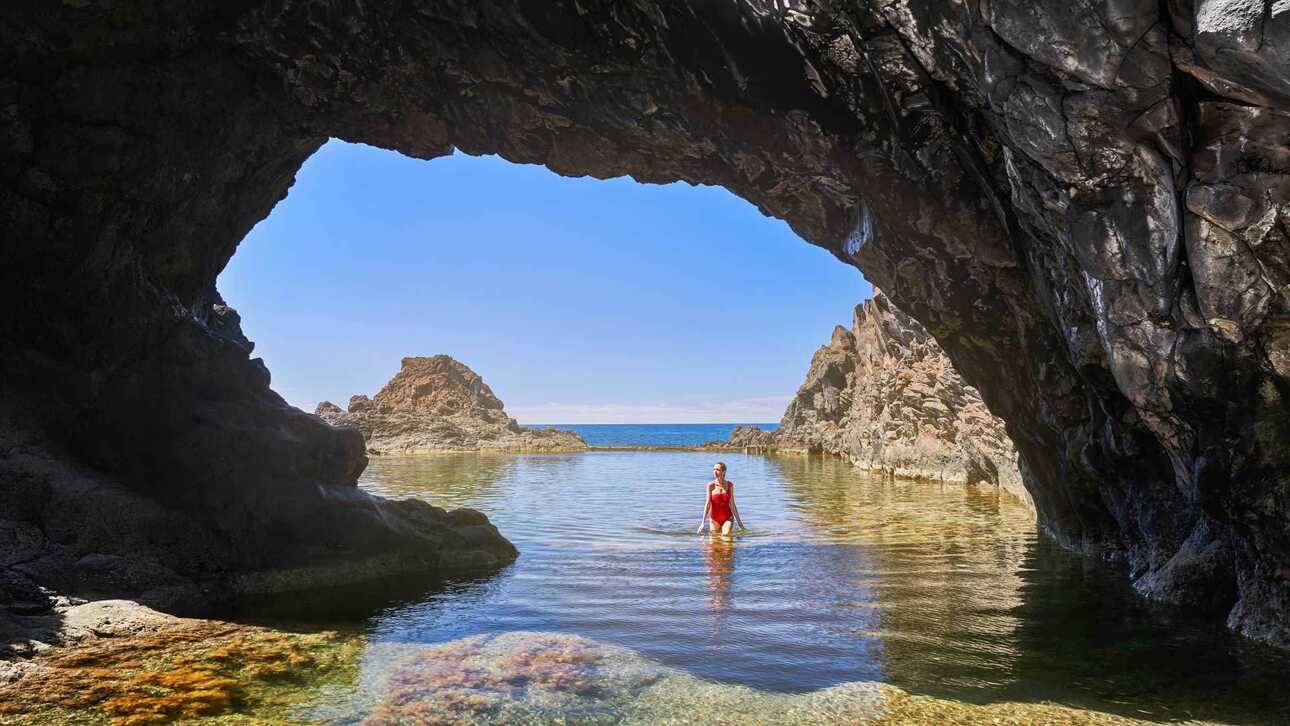 Frau im Naturpool von Seixal vor dunklen Felsen und türkisblauem Meer.