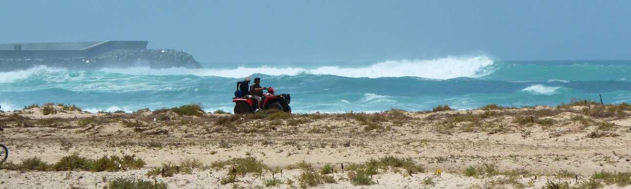 Ein Quad fährt entlang der Küste, im Hintergrund tosende Wellen