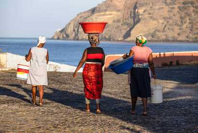 Drei kapverdische Frauen mit Schüsseln und Eimern gehen am Strand entlang