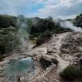 Dampf steigt aus einer heißen Schwefelquelle im Kurort Furnas auf São Miguel empor, umgeben von grünen Hügeln.