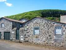 Traditionelles Natursteinhaus der Quinta dos Frutos auf den Azoren vor grün bewaldetem Hügel in ruhiger Lage
