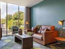 Octant Hotel Furnas – stilvolles Wohnzimmer mit moderner Einrichtung und großem Fenster mit Ausblick auf grüne Landschaft auf Sao Miguel.