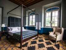 Elegantes, koloniales Schlafzimmer mit Himmelbett und gemütlichem Sessel – stilvoll wohnen auf Ihrer picotours-Reise.