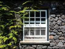 Qunita dos Frutos auf Graciosa, malerisches Fenster in traditioneller Steinfassade mit lebendigem Grün.