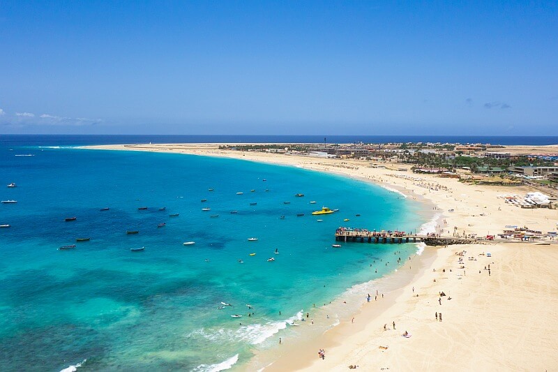 Langer Sandstrand mit Holzsteg und türkisfarbenem Meer in Santa Maria auf der Insel Sal, Kapverden.