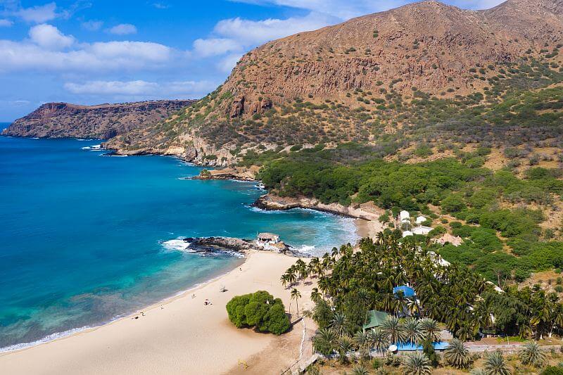 Feinsandiger Strand mit Palmen und türkisblauem Wasser in Tarrafal auf Santiago, Kapverden, eingerahmt von Bergen.